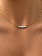 Close-up of a gold necklace with four 4 mm grey baroque freshwater pearls worn on the neck.