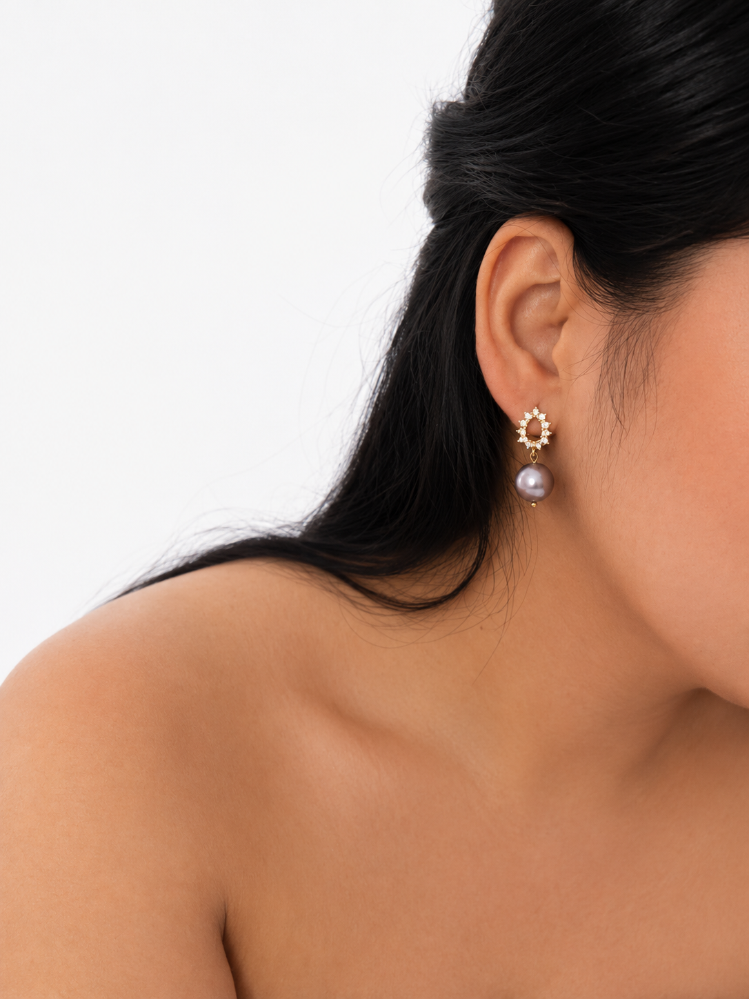 Woman wearing a gold halo drop earring with a grey baroque freshwater pearl and clear stone setting