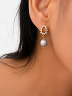 Close-up of a gold halo earring with a grey baroque freshwater pearl and clear stones worn on the ear