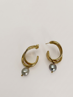 Woman wearing a sculptural gold hoop earring with a grey baroque freshwater pearl drop.