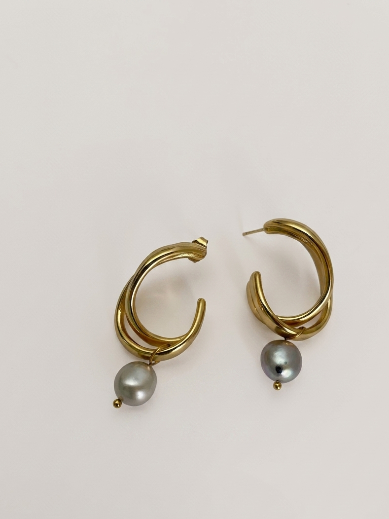 Woman wearing a sculptural gold hoop earring with a grey baroque freshwater pearl drop.