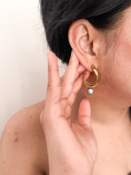 Angled close-up of sculptural gold hoop earrings with organic grey freshwater pearl drops.