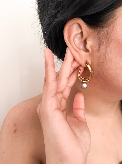 Angled close-up of sculptural gold hoop earrings with organic grey freshwater pearl drops.
