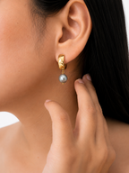 Close-up of a gold huggie earring with a grey baroque freshwater pearl drop worn on the ear.