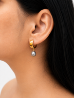 Woman wearing a polished gold huggie hoop earring with a grey baroque freshwater pearl drop