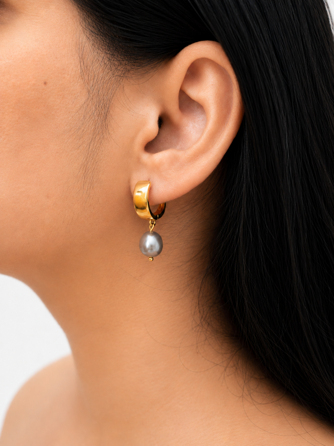Woman wearing a polished gold huggie hoop earring with a grey baroque freshwater pearl drop