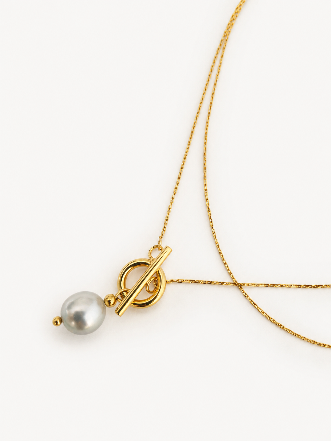 Close-up of a gold lariat necklace with a 10 mm grey baroque freshwater pearl pendant and toggle detail.