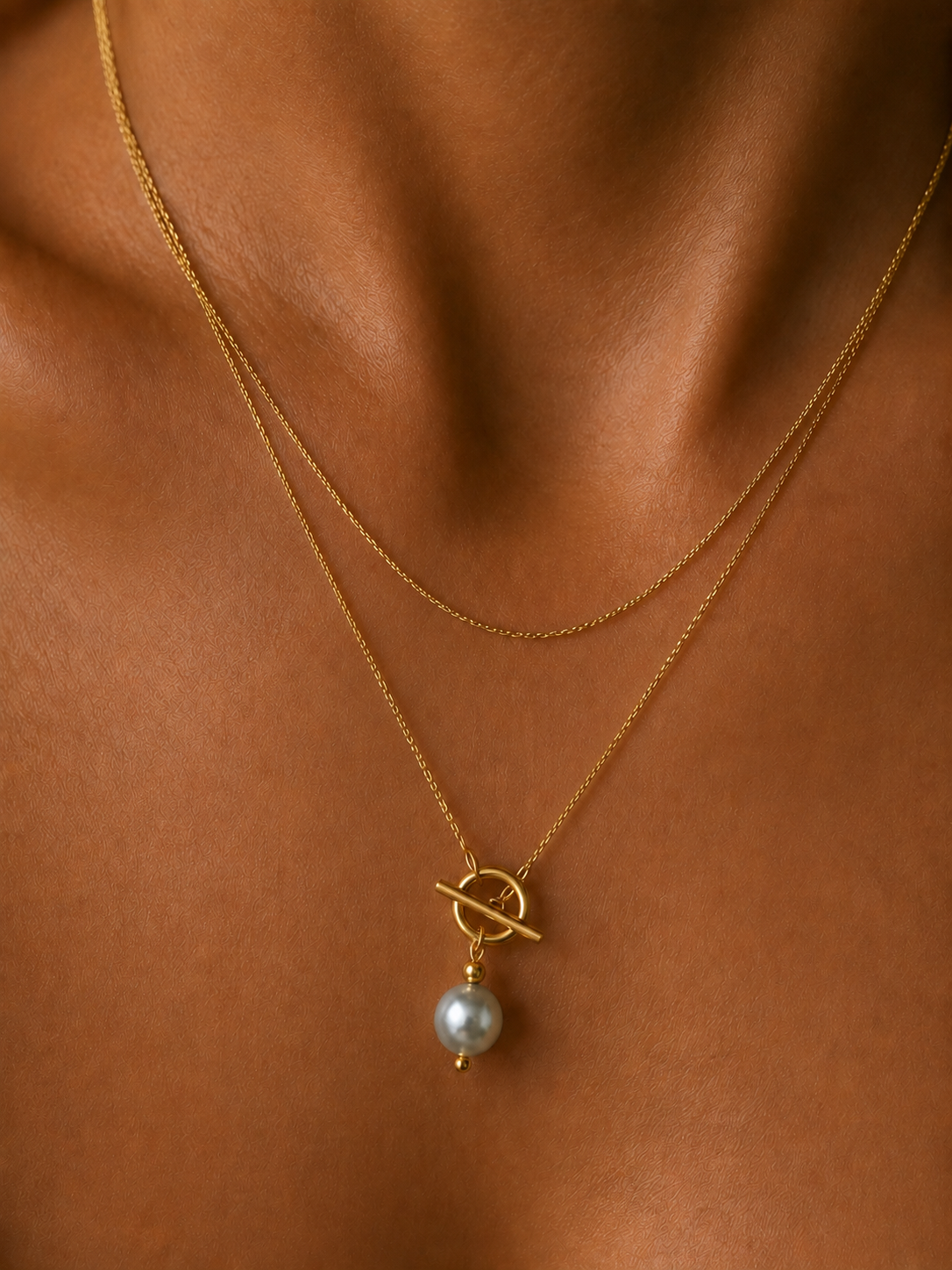 Close-up of a gold lariat Y-necklace with a 10 mm grey baroque freshwater pearl and toggle detail worn on the neck.