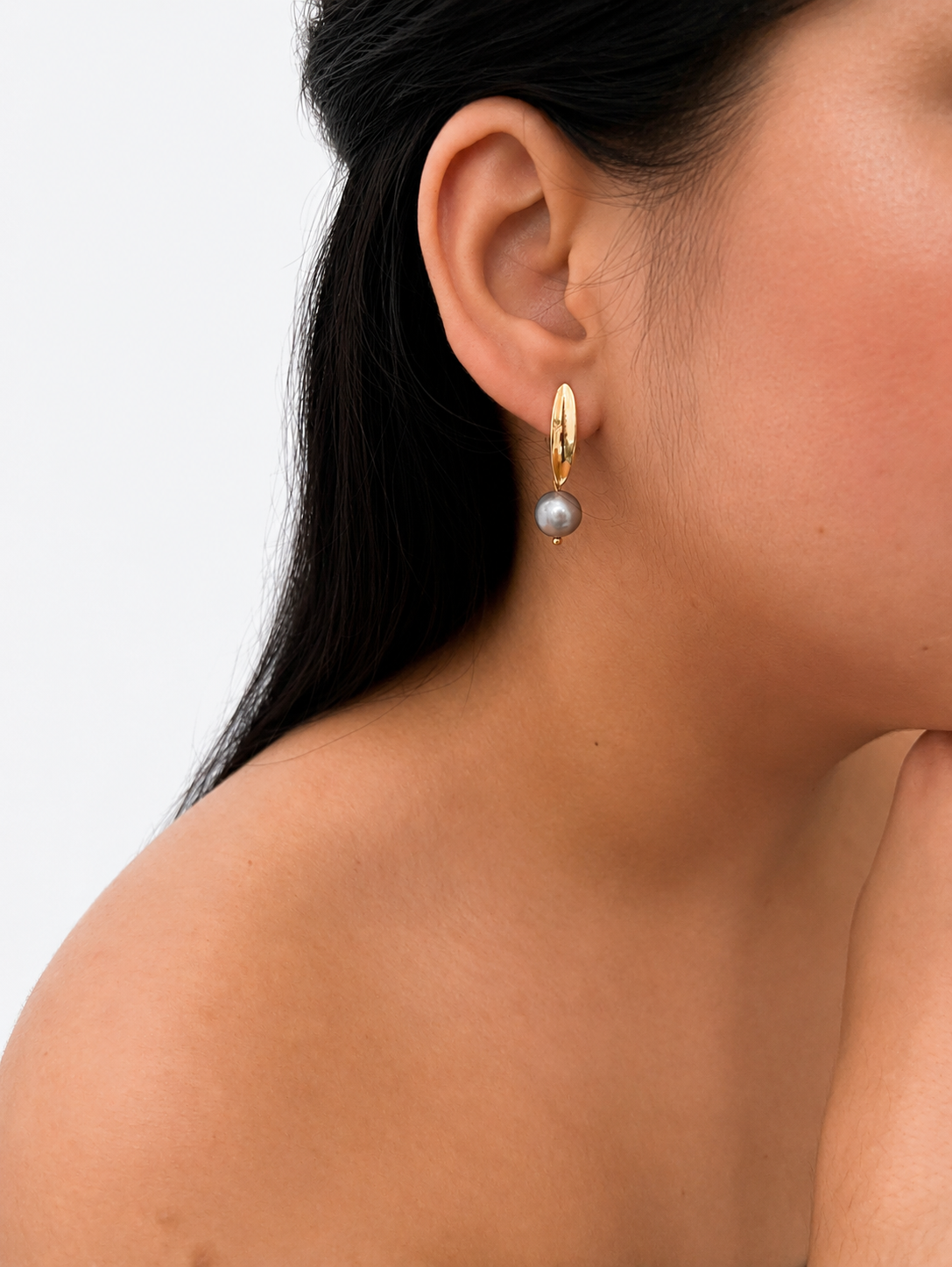 Woman wearing a gold leaf drop earring with a grey baroque freshwater pearl.