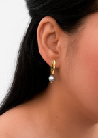 Close-up of a gold pandan leaf earring with a grey baroque freshwater pearl worn on the ear.
