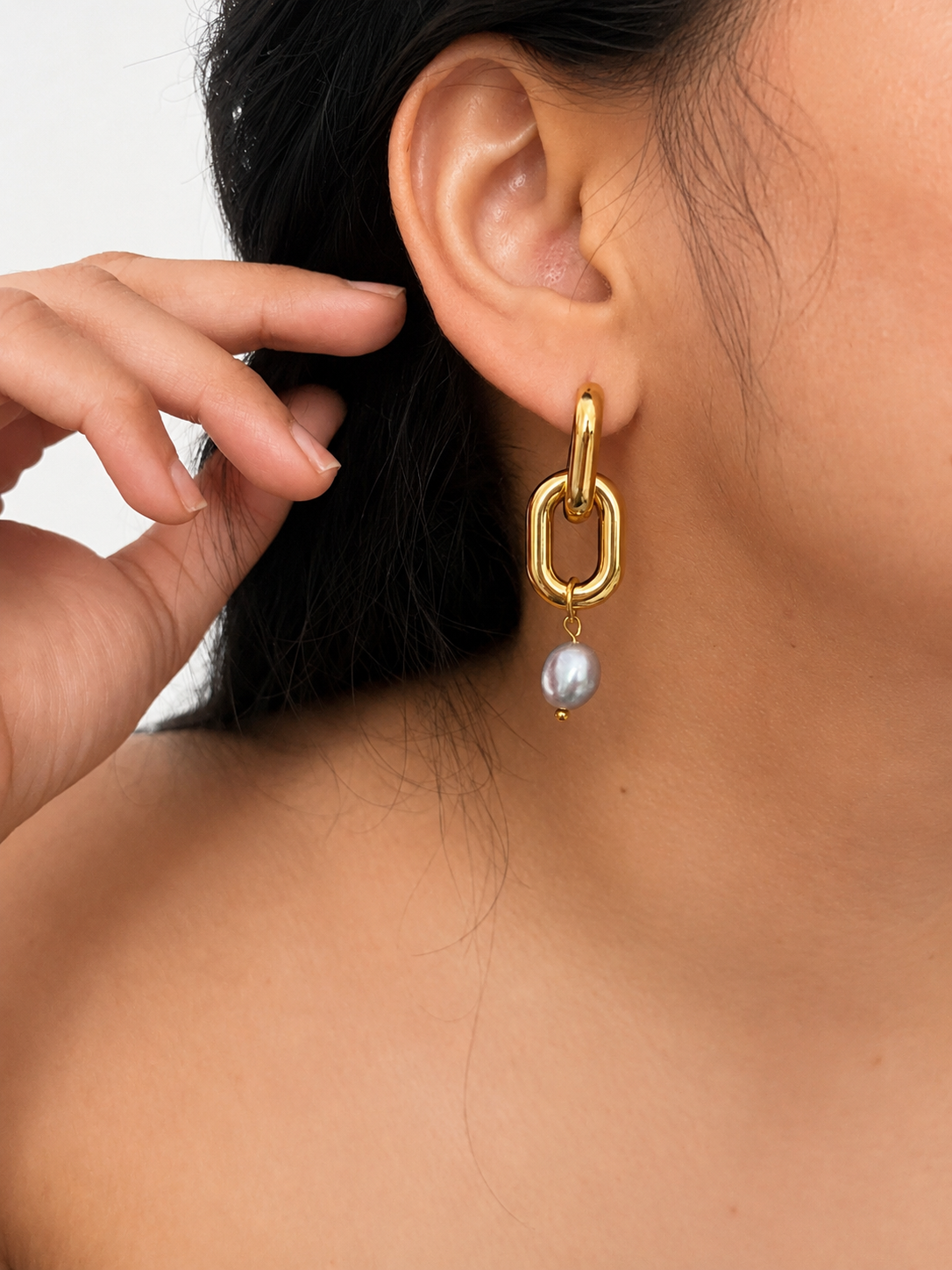 Close-up of a gold link drop earring with a grey baroque freshwater pearl worn on the ear.