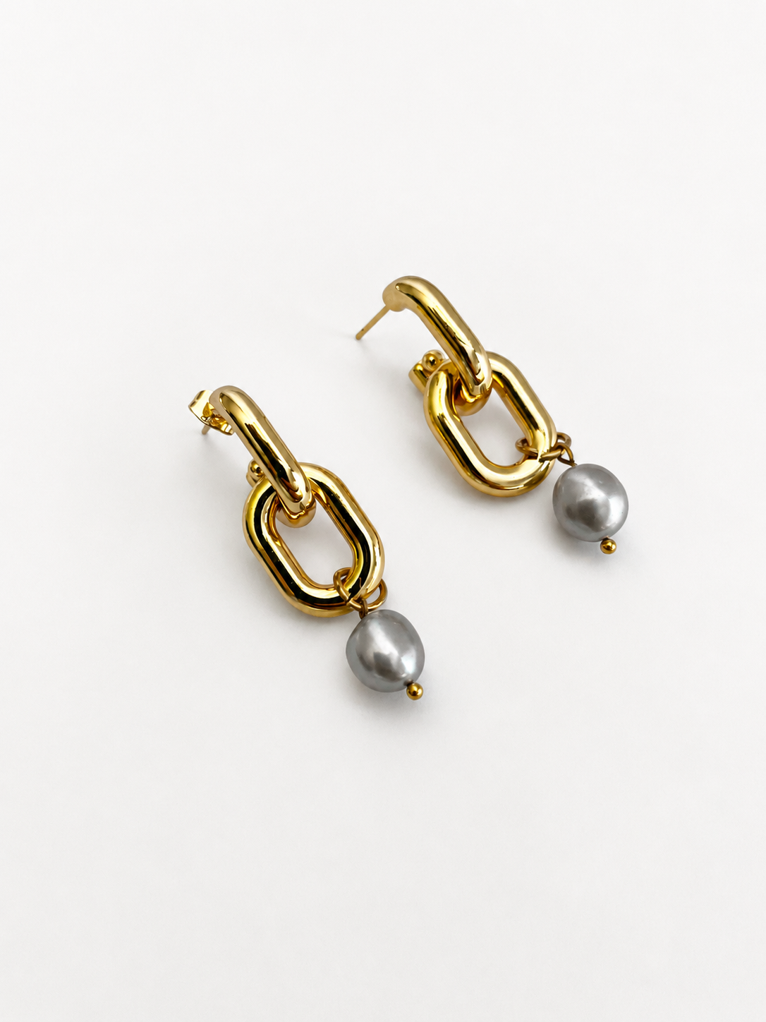 Angled close-up of gold link earrings with organic grey baroque freshwater pearl drops.