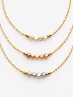 White, pink and grey baroque freshwater pearl necklaces with elongated gold chains and bead accents.