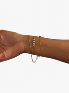 Grey baroque freshwater pearl necklace styled around the wrist with layered gold chains.