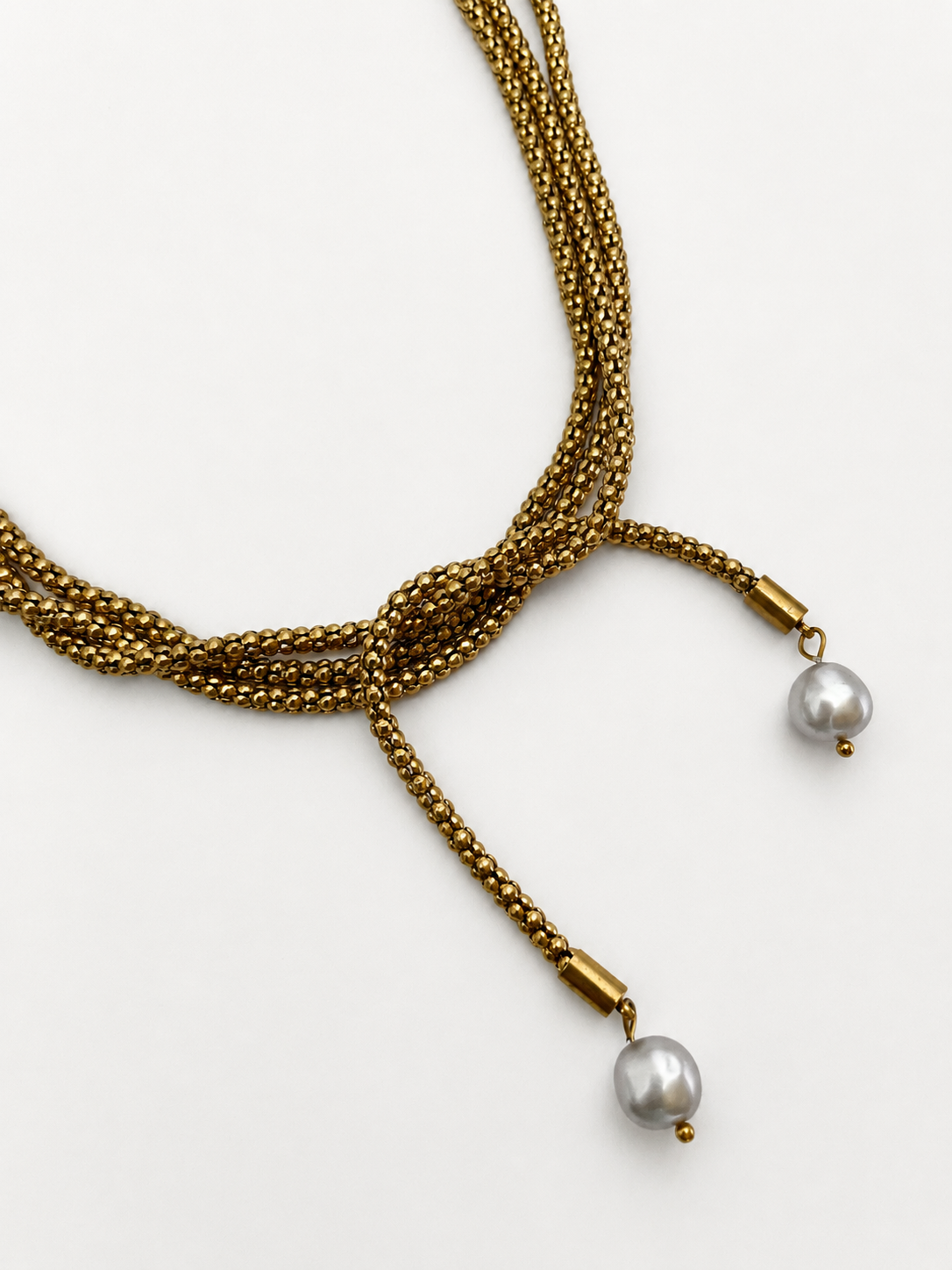 Close-up of a knotted gold open beaded necklace with two grey baroque freshwater pearl drops.