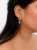 Close-up of a gold pebble drop earring with a grey baroque freshwater pearl worn on the ear.