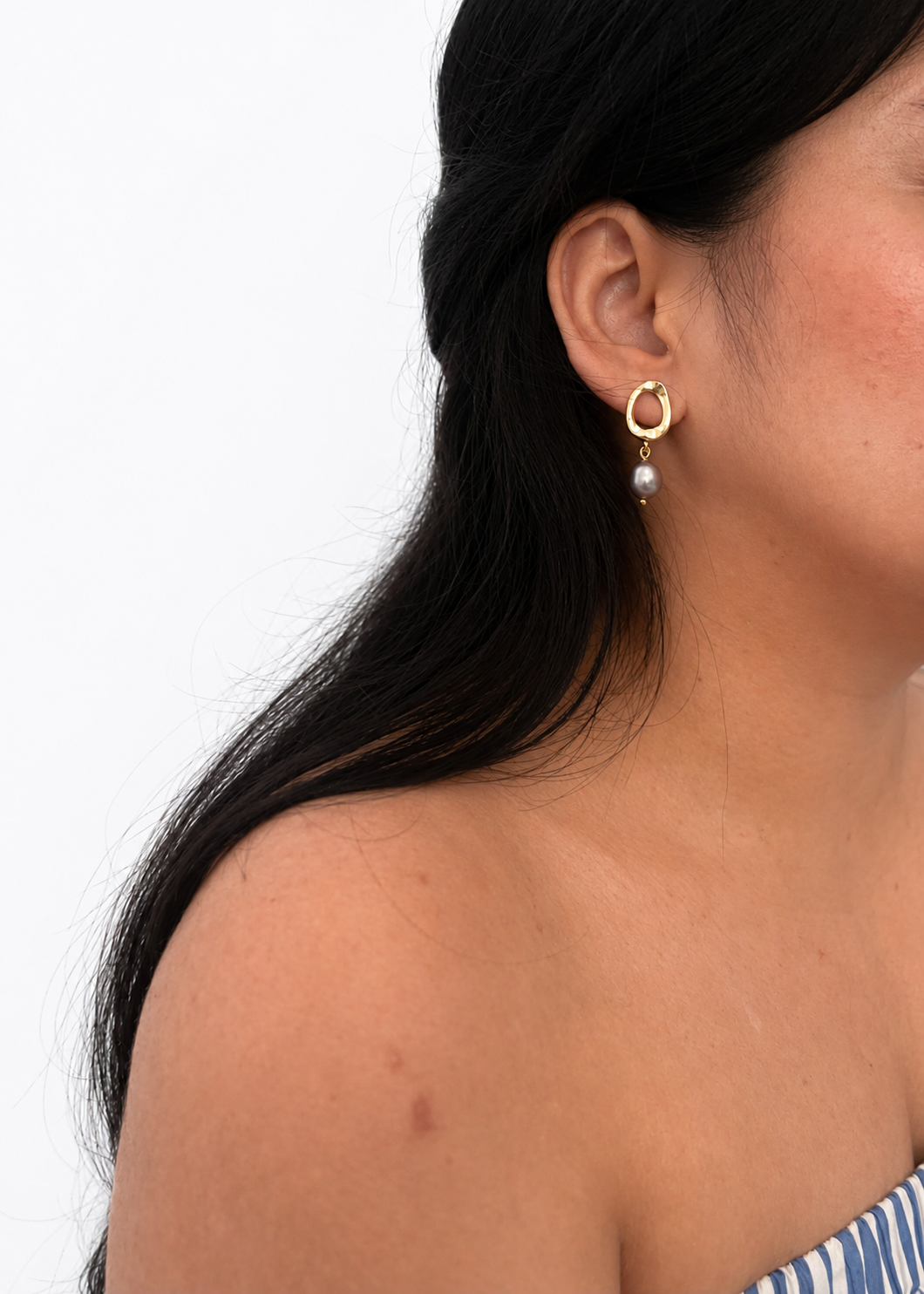 Woman wearing a gold pebble drop earring with a grey baroque freshwater pearl