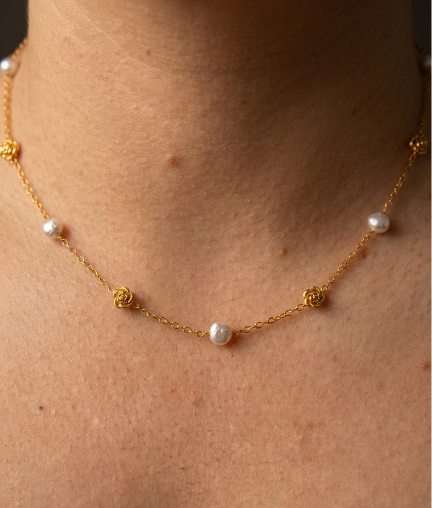 Close-up of a gold rose station necklace with grey baroque freshwater pearls worn on the neck