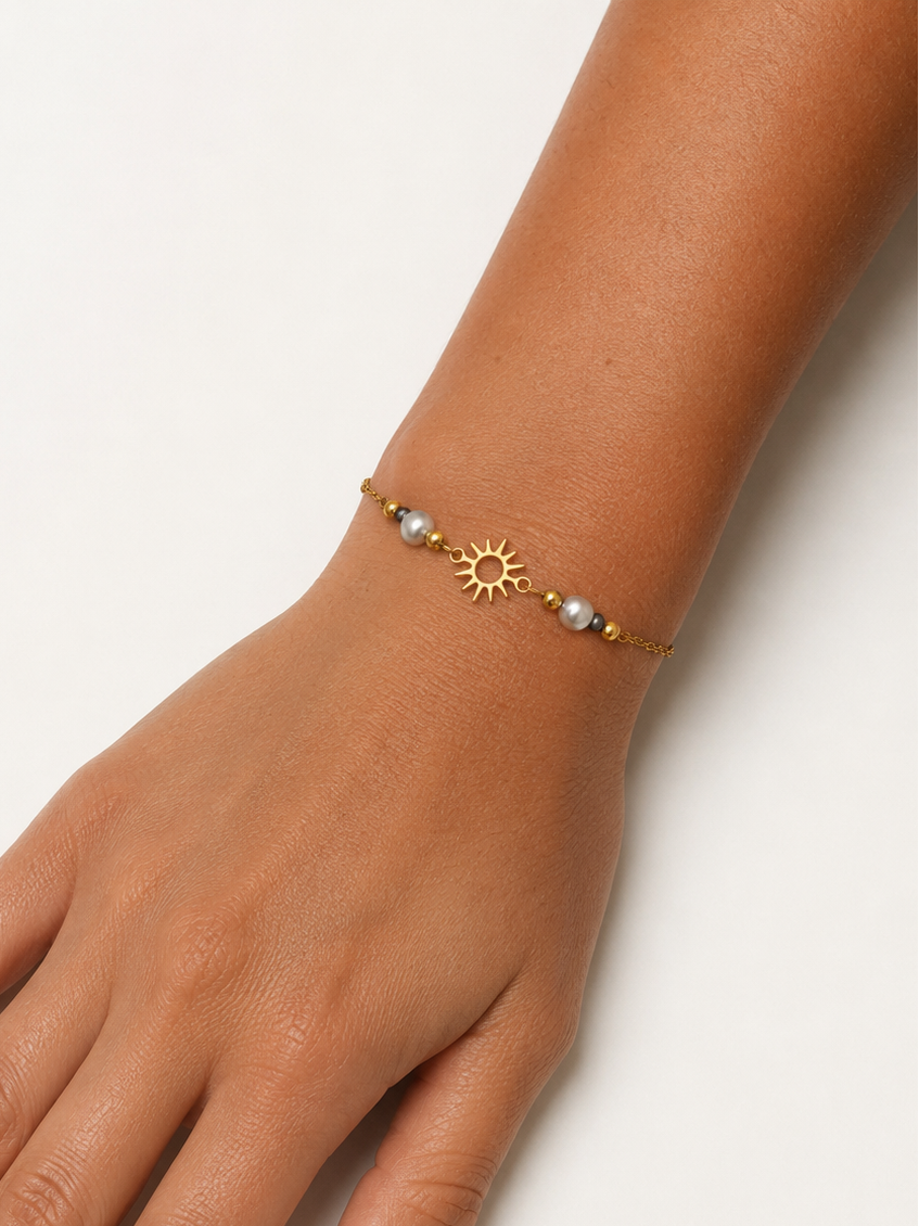 Close-up of a gold sun charm bracelet with grey baroque freshwater pearls and small gold beads on the wrist