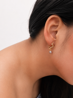 Close-up of a gold Waves petit creole earring with a grey baroque freshwater pearl worn on the ear.