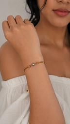 Woman wearing a chunky gold bracelet with an oval grey freshwater pearl and polished gold bead accents