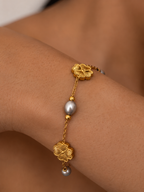 Close-up of a gold clover bracelet with grey freshwater pearls and polished gold beads on the wrist