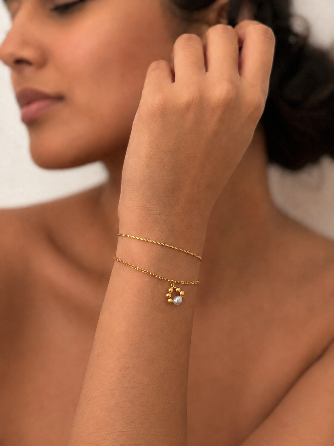Woman wearing a gold double-chain bracelet with a petite grey freshwater pearl and polished gold beads
