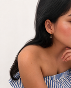 Woman wearing a gold half moon huggie earring with a 6 mm oval grey freshwater pearl drop