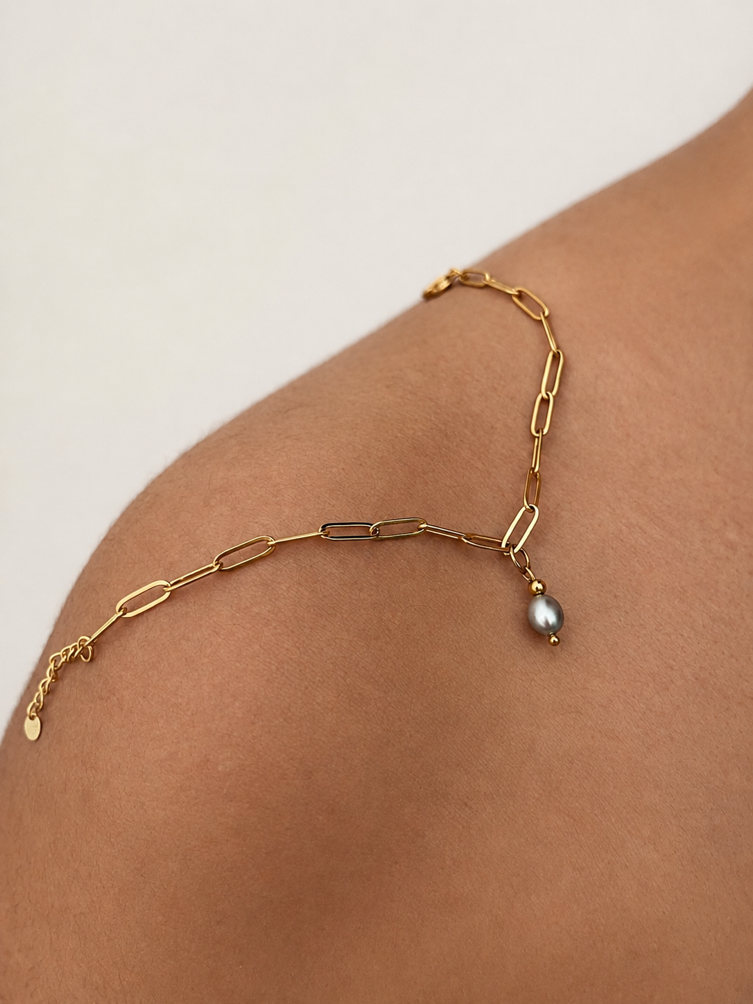 Close-up of a gold paperclip-chain bracelet with a grey pearl drop and adjustable extender
