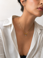 Woman wearing a gold Ripple necklace with a grey freshwater pearl pendant and sculptural ring details
