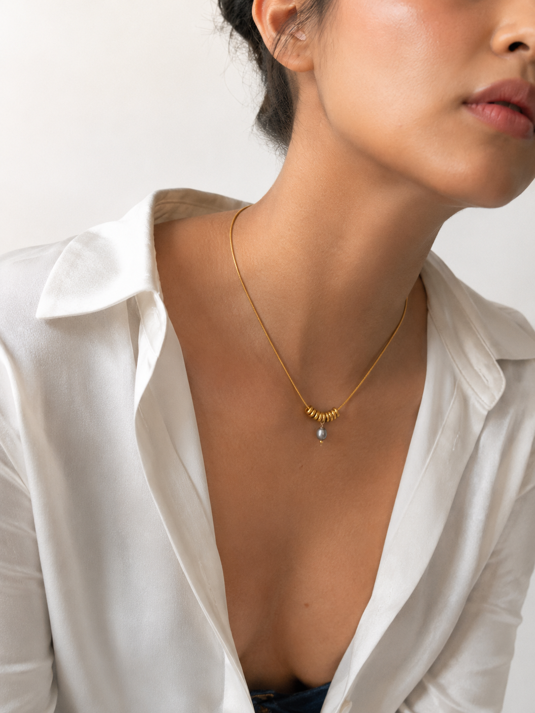 Woman wearing a gold Ripple necklace with a grey freshwater pearl pendant and sculptural ring details