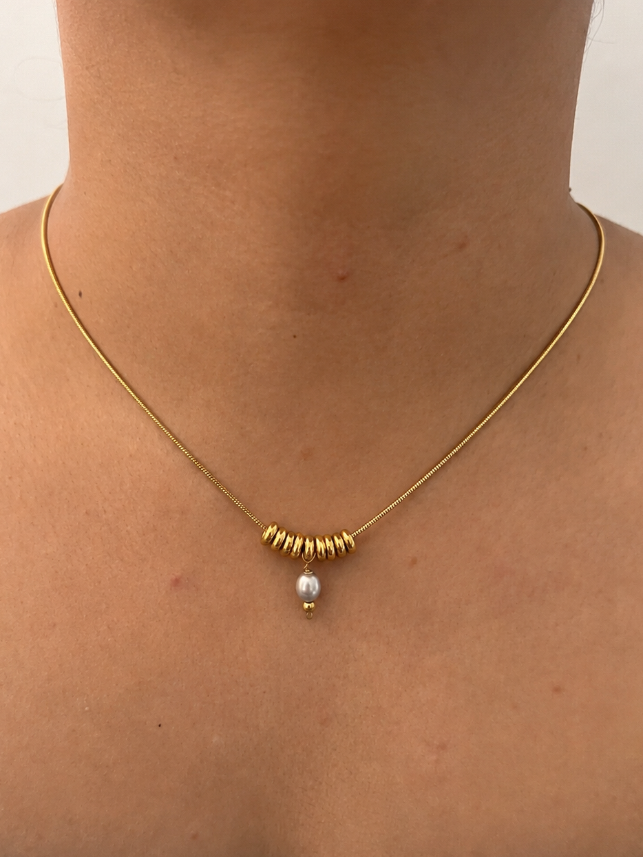 Front view of a gold Ripple necklace with a grey freshwater pearl pendant and polished gold ring accents