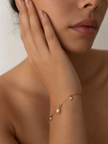 Woman wearing a gold charm bracelet with a grey freshwater pearl and two clear stone accents