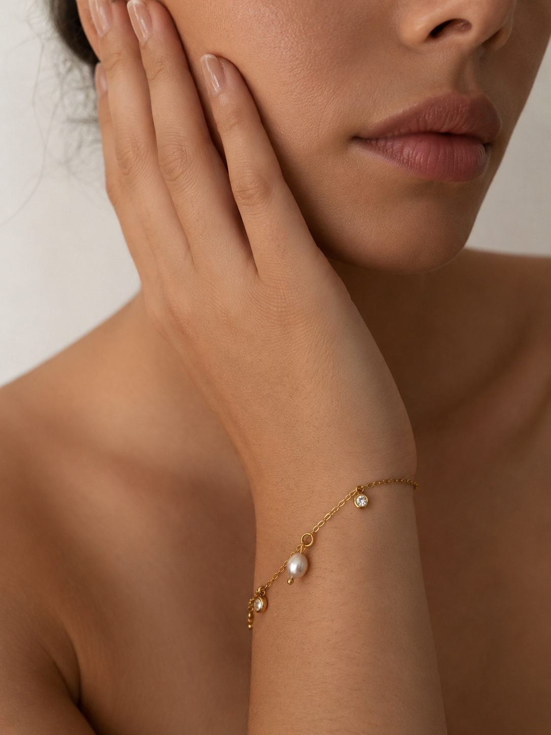 Woman wearing a gold charm bracelet with a grey freshwater pearl and two clear stone accents