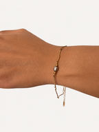 Close-up of a gold wave-chain bracelet with a grey freshwater pearl and polished gold beads on the wrist