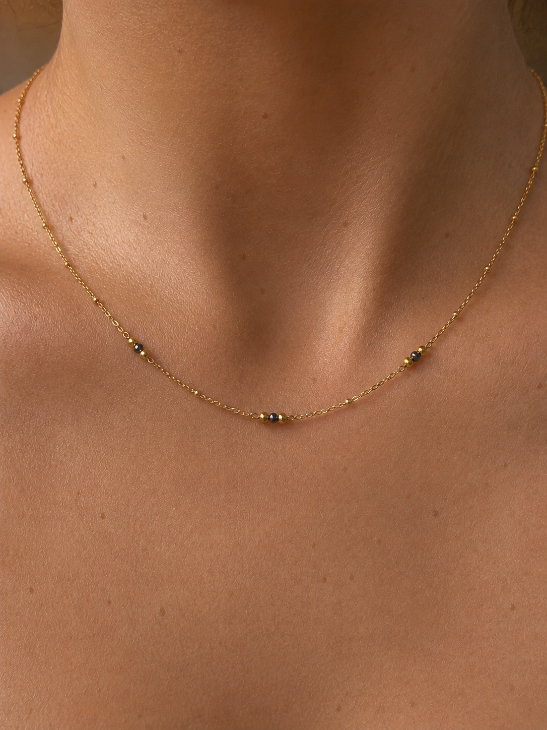 Close-up of a delicate gold necklace with 2 mm grey Keshi freshwater pearls and polished gold bead accents.