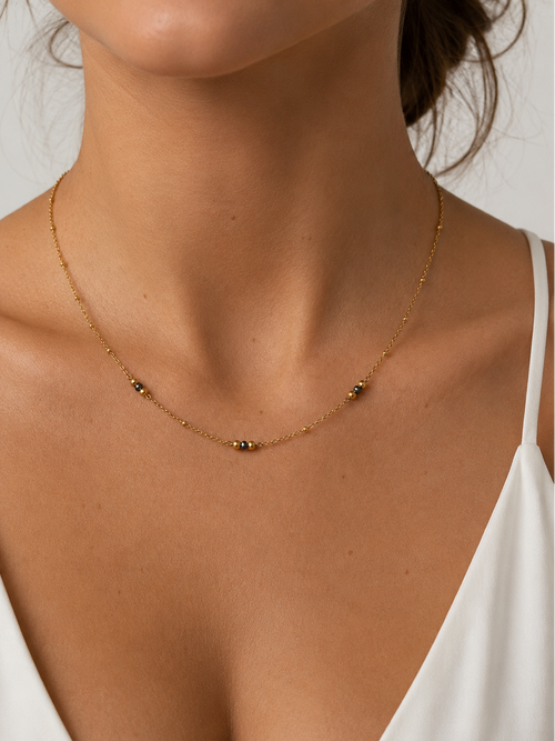 Woman wearing a delicate gold necklace with 2 mm grey Keshi freshwater pearls and gold bead accents.