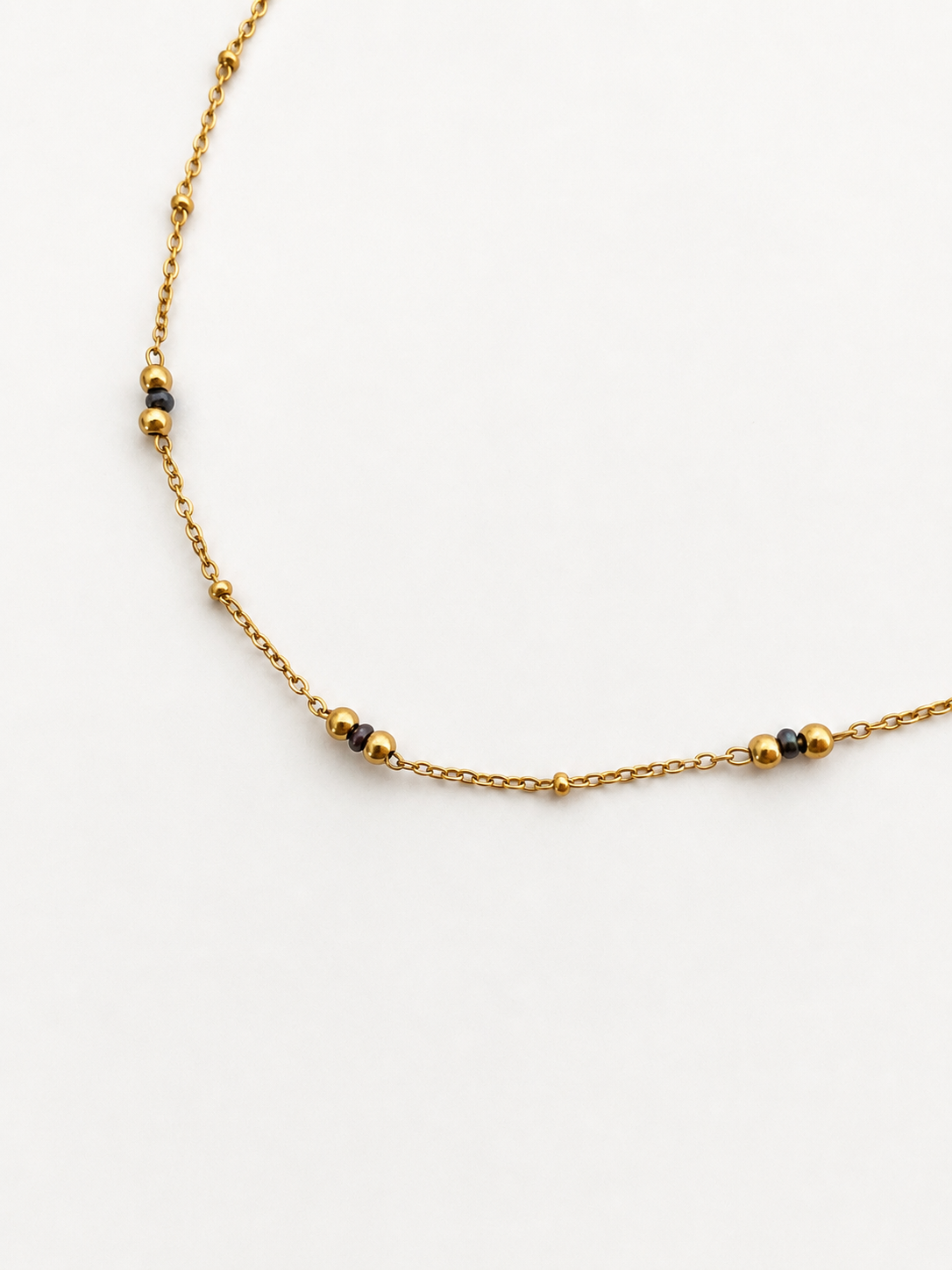 Close-up of a delicate gold chain necklace with grey Keshi freshwater pearls framed by polished gold beads.