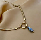 flat gold herringbone chain necklace featuring a front toggle clasp and an elongated grey keshi pearl pendant, styled with a deep V-neck ivory silk top