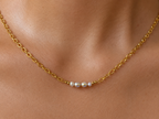 Close-up of a gold statement necklace with two 6 mm oval and two 4 mm baroque grey freshwater pearls worn on the neck