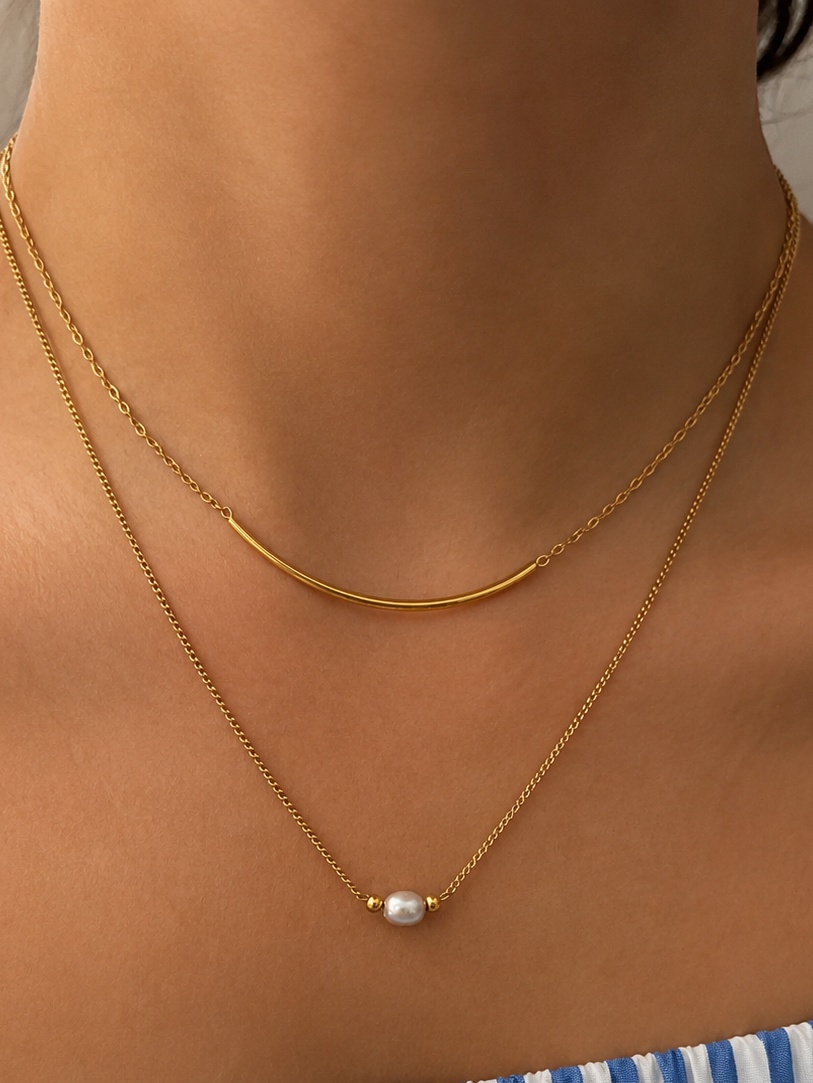 Close-up of a layered gold necklace with a 6 mm oval grey freshwater pearl and curved arc detail worn on the neck