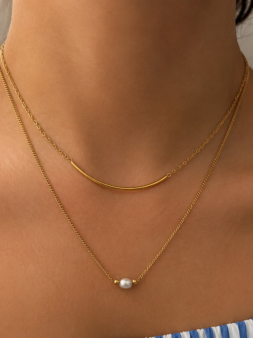 Close-up of a layered gold necklace with a 6 mm oval grey freshwater pearl and curved arc detail worn on the neck