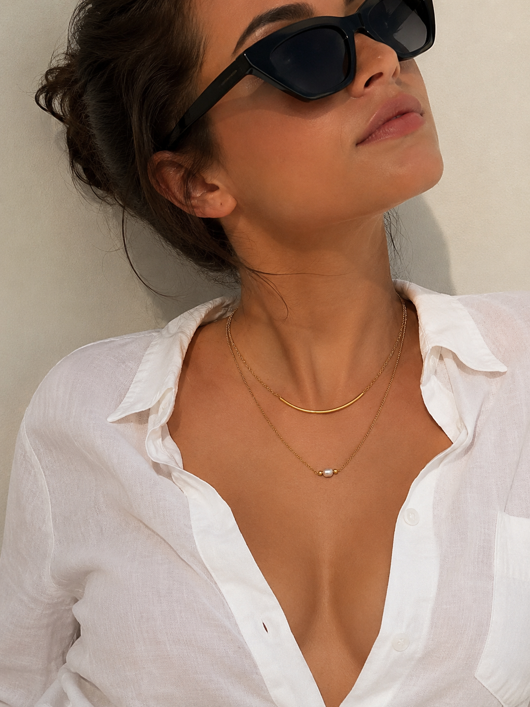 Woman wearing a layered gold necklace with a 6 mm oval grey freshwater pearl and sculptural arc detail