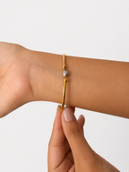 Close-up of a chunky gold bracelet with a 6 mm oval grey cultured freshwater pearl worn on the wrist.