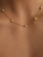 Close-up of a gold Clover Bloom necklace with 6 mm grey oval freshwater pearls and clover details worn on the neck.