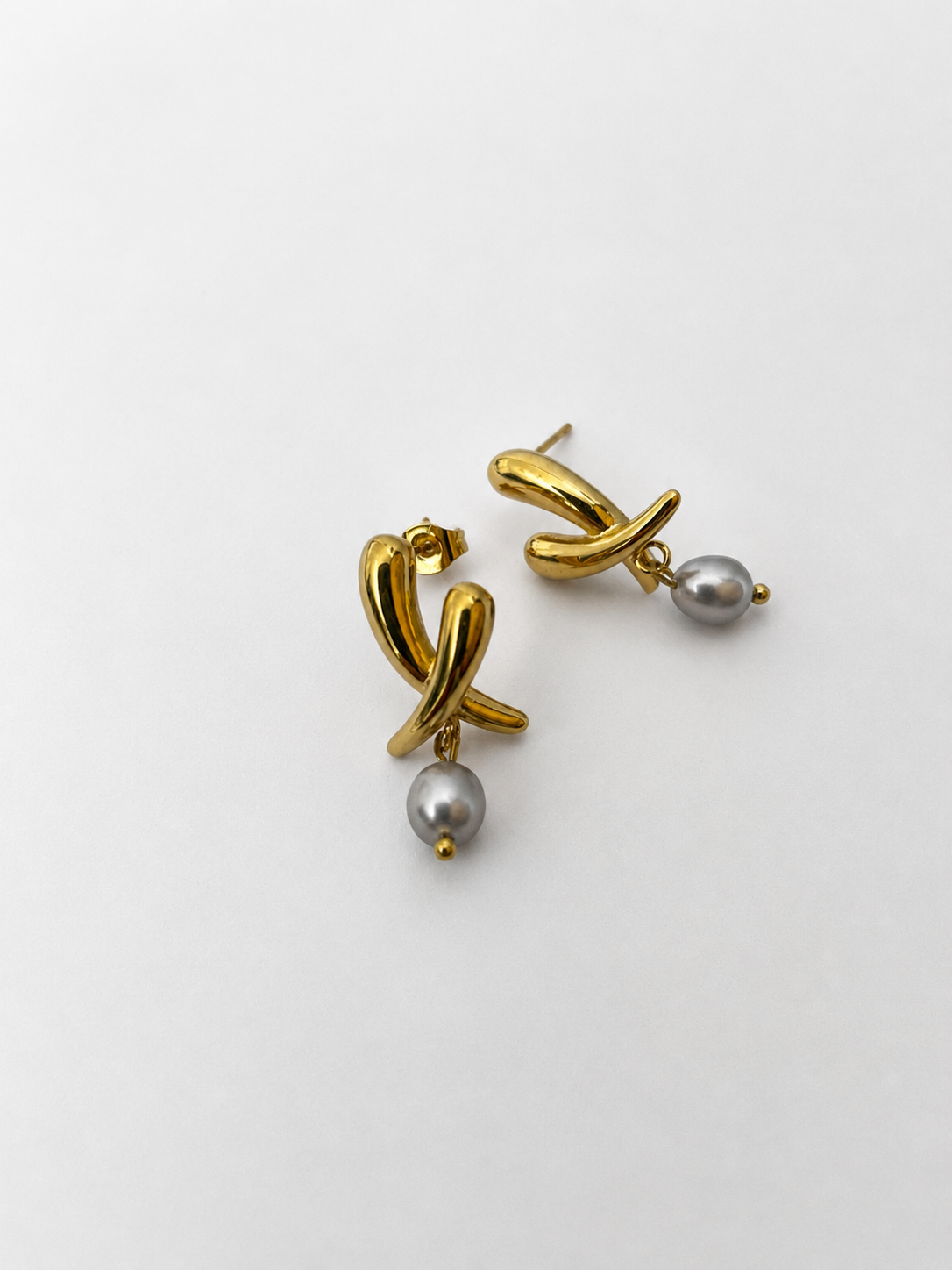 Pair of sculptural gold cross stud earrings with 6 mm oval grey freshwater pearl drops.