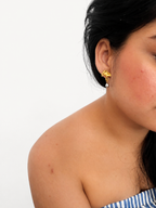 Woman wearing a gold ginkgo leaf drop earring with an oval grey freshwater pearl.