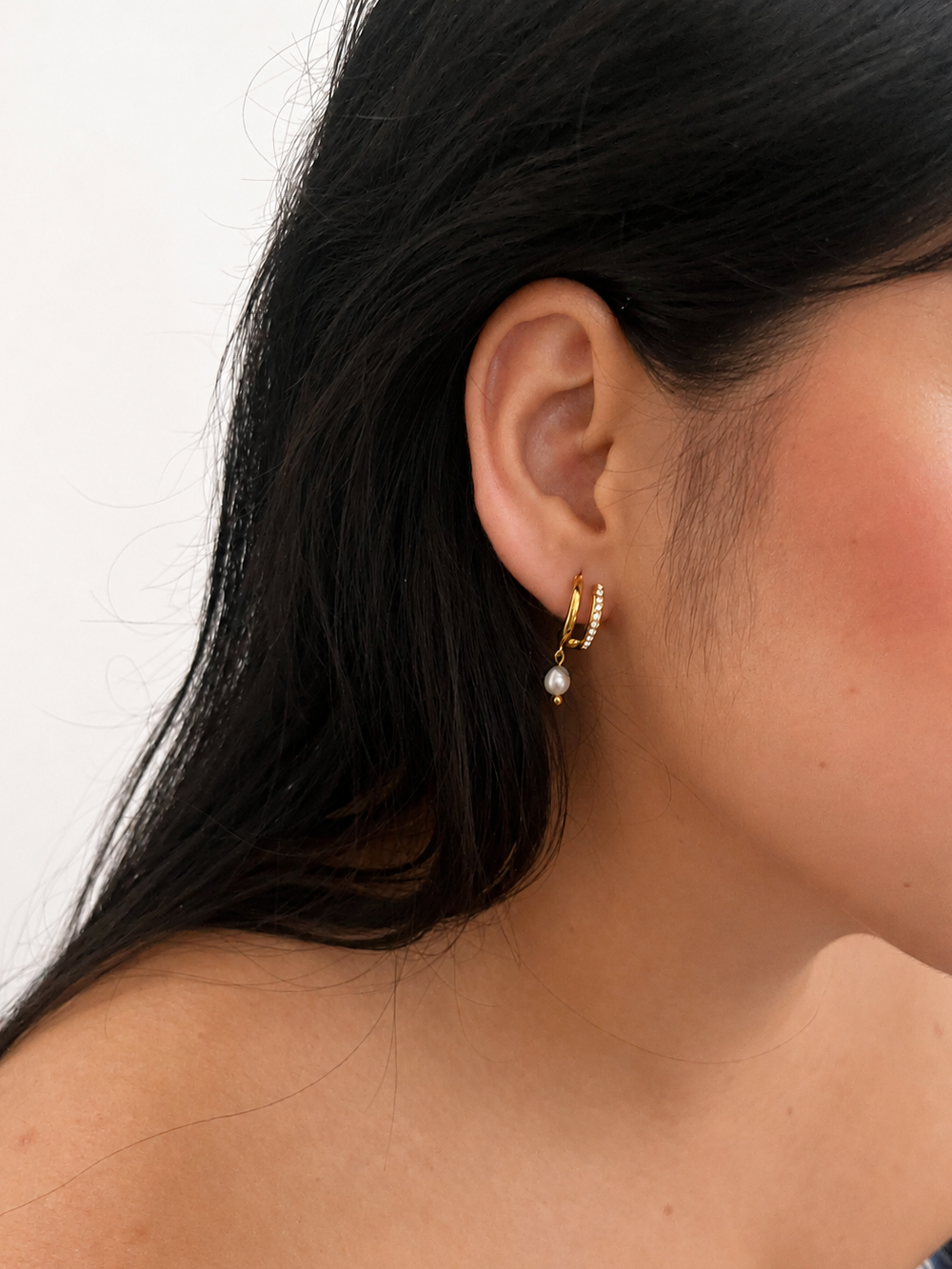 Close-up of a gold half moon huggie earring with a grey freshwater pearl and cubic zirconia worn on the ear