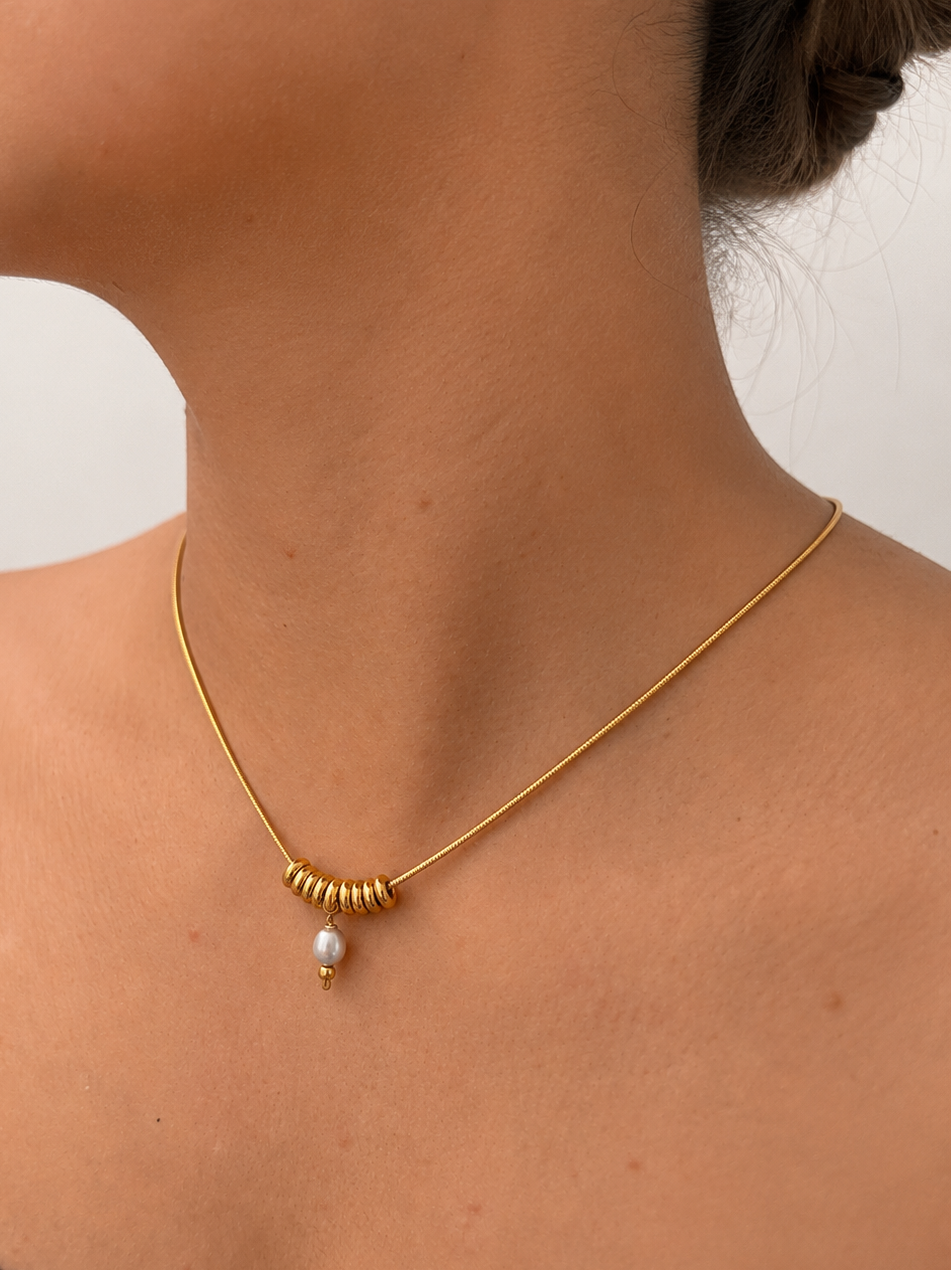 Close-up of a gold Ripple necklace with a 6 mm grey freshwater pearl and polished ring accents worn on the neck