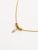 Close-up of a gold Ripple necklace with a 6 mm grey freshwater pearl pendant and polished ripple-style rings.
